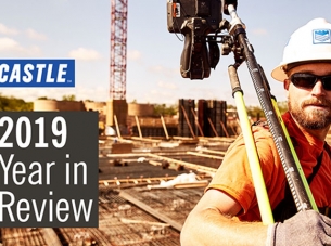 Castle construction worker wearing orange shirt and white hardhat carries equipment over his shoulder