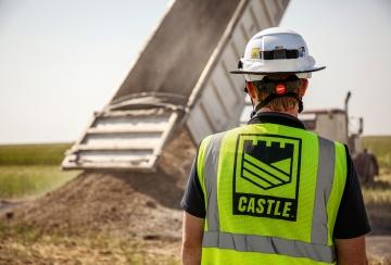 Construction worker in Castle PPE in front of dump truck