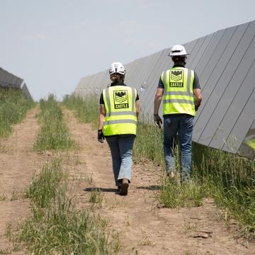 Two people in Castle PPE walking along solar panel row