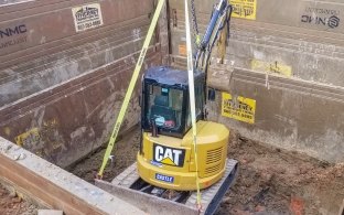 CAT yellow excavator lowered in utilities pit