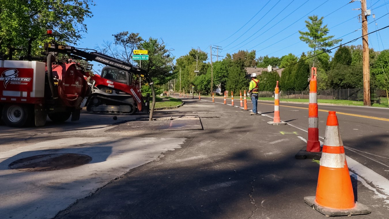 orange traffic cones, construction worker, and excavation machines on residential road