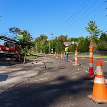 orange traffic cones, construction worker, and excavation machines on residential road